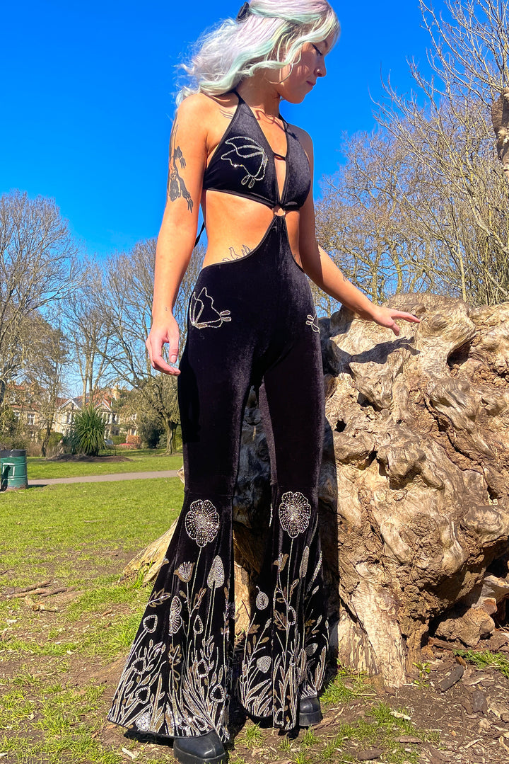 Side view of The Fairy Garden Catsuit outdoors, featuring halter cut-out top and sequin floral flares. Rave-ready velvet one-piece.