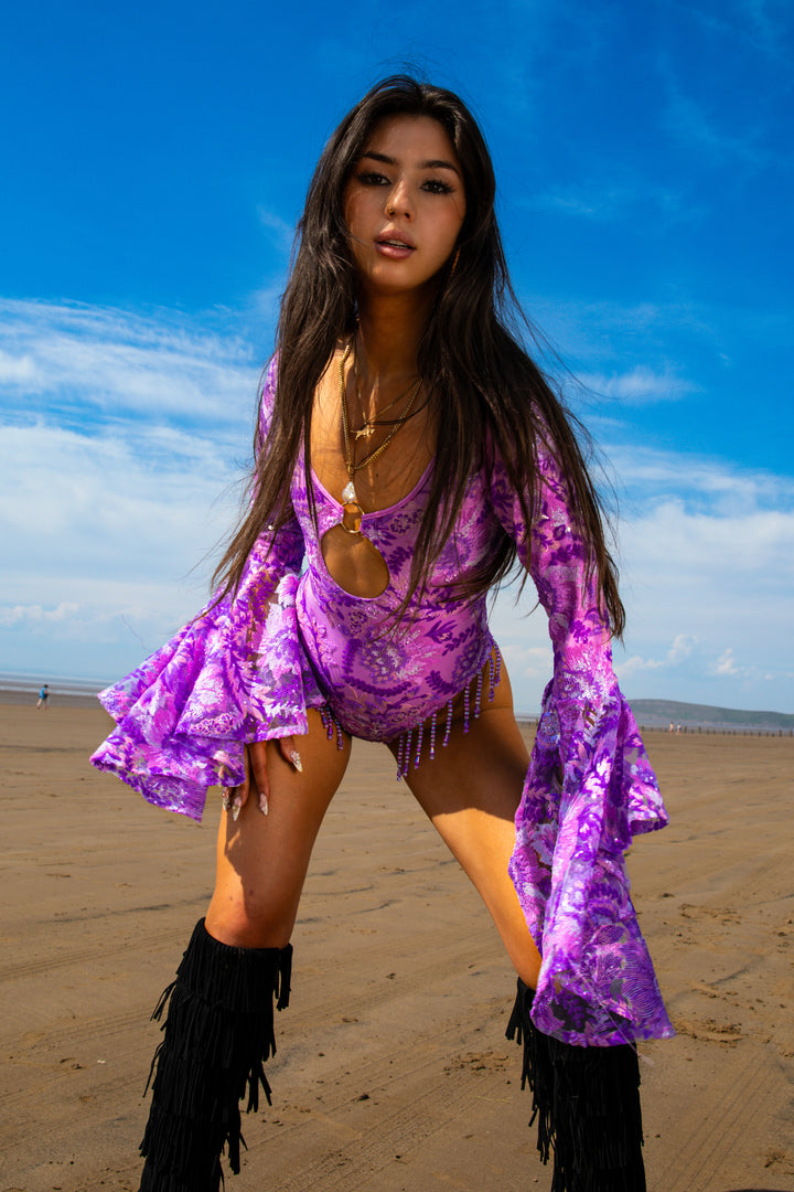 Model wears Wild Like Me Flared Bodysuit with fringe details and flared sleeves, styled with black fringe boots for festival-ready look.