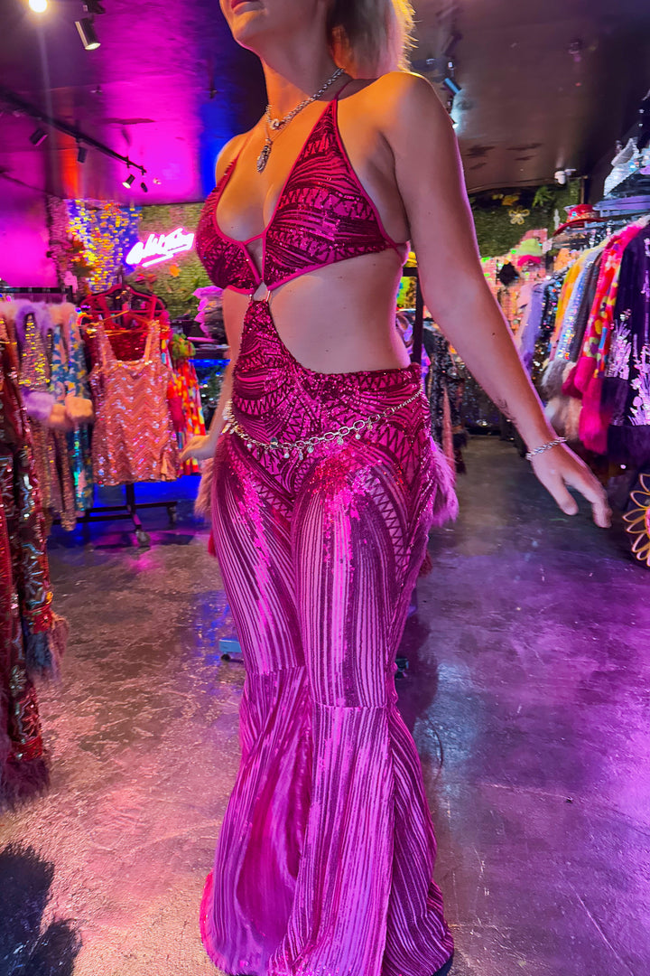 Model wearing the pink Sabrina Sequin Catsuit in a boutique setting, showcasing its vibrant sparkle and flared silhouette.