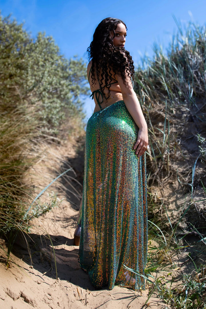 Back view of Emerald Maxi Dress in natural setting, showcasing sequin flow and open-back design for rave wear.