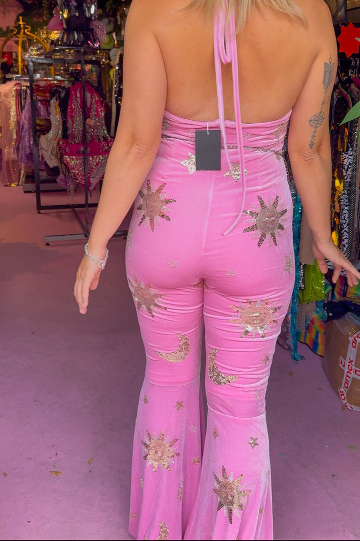Rear view of The Phase Catsuit Pink - Stretch velvet catsuit with open back, celestial gold sequins, and flared legs in boutique display.
