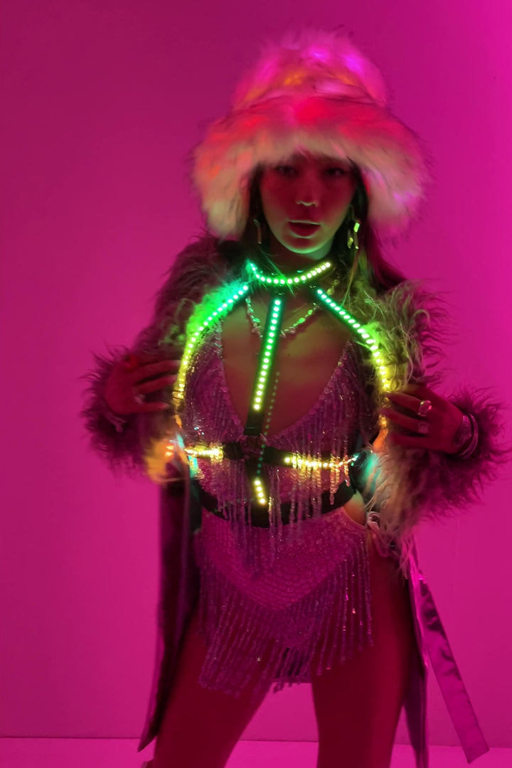 Afterglow Cross LED Harness in green and yellow over rhinestone fringe bodysuit and faux fur coat. Glow Up Bikini Harness by Wild Thing.