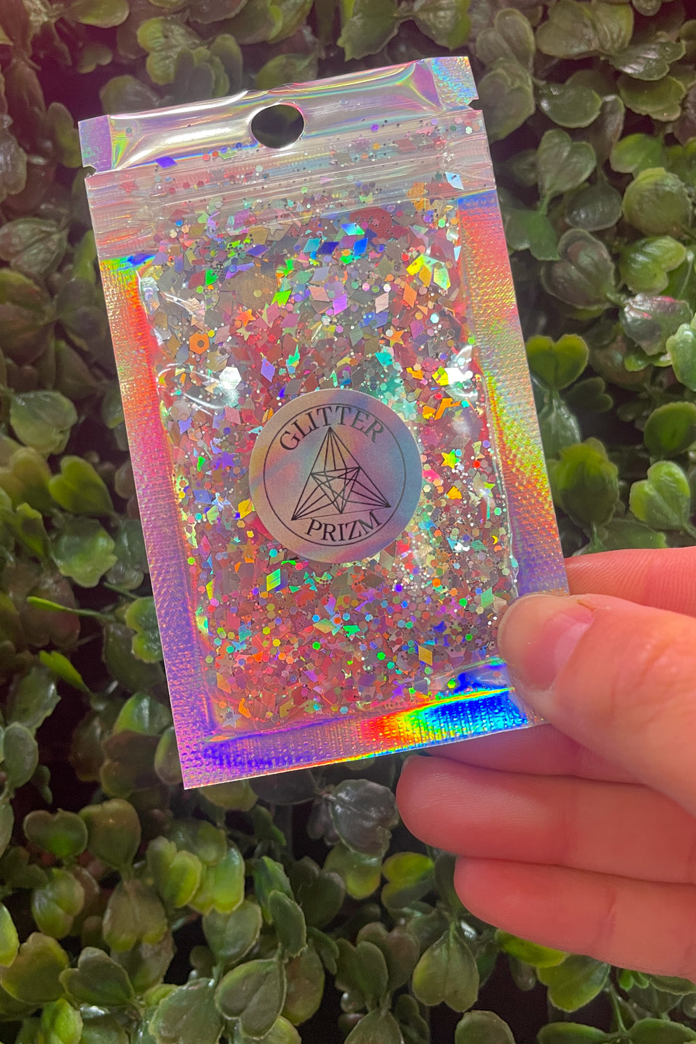 Glitterprizm holographic glitter bag held against greenery