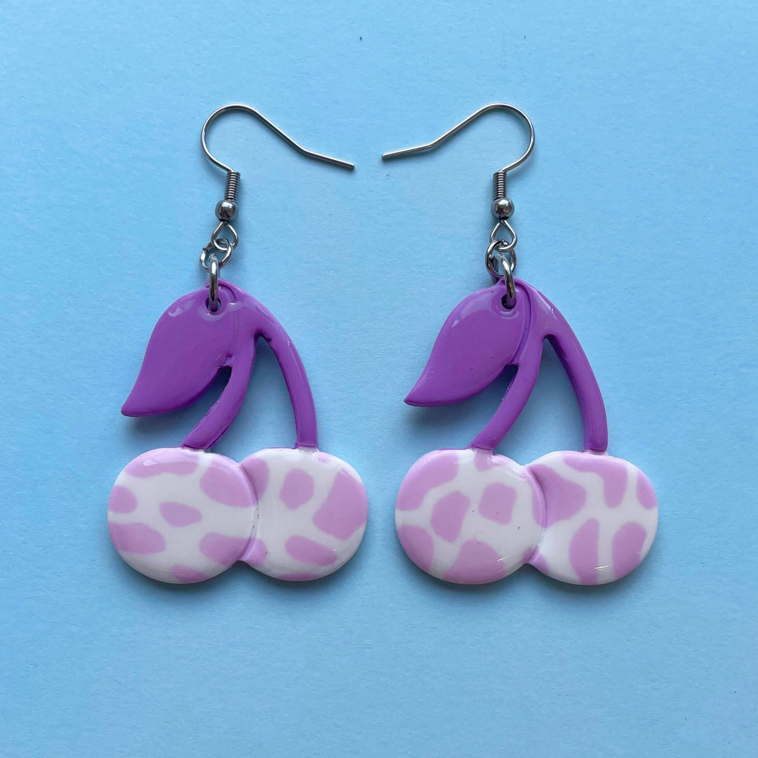 Purple cow print cherry earrings on blue background