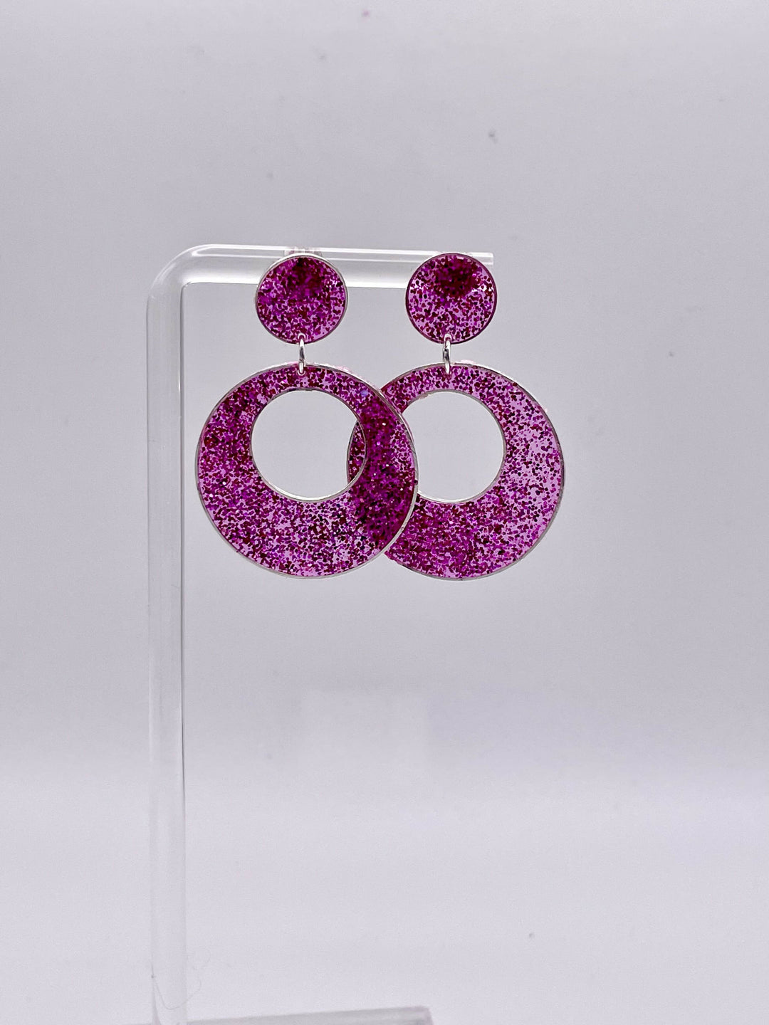 Sparkly pink resin earrings displayed on a stand