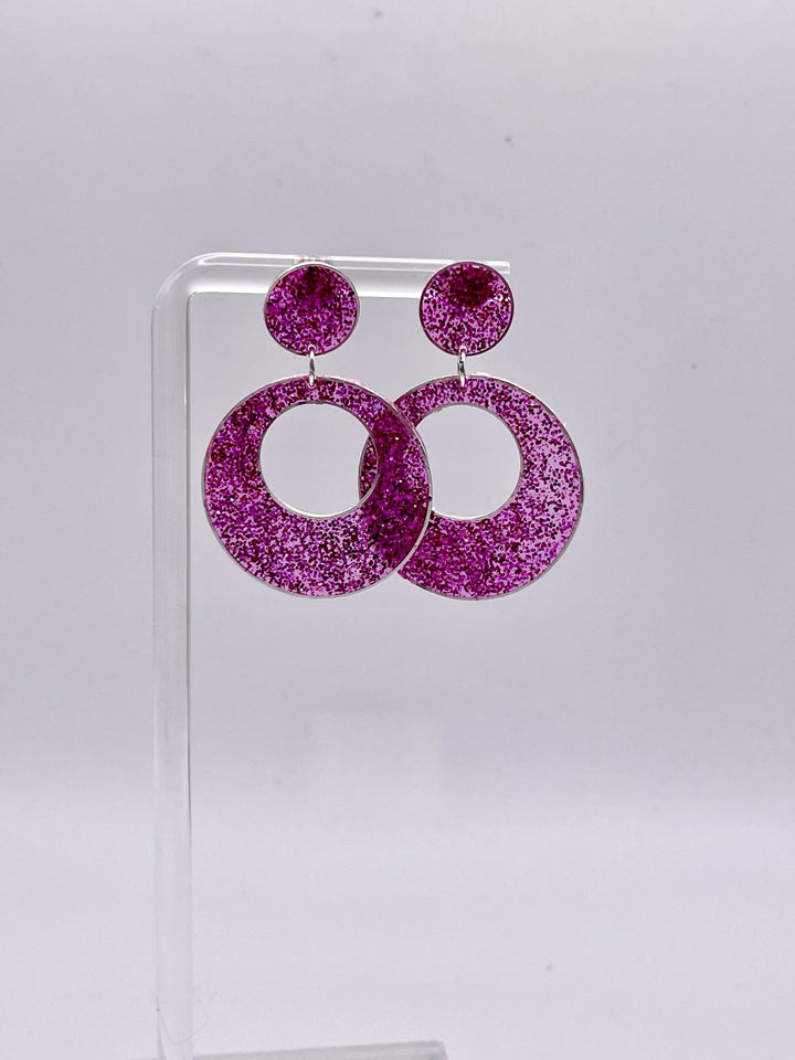 Sparkly pink resin earrings displayed on a stand