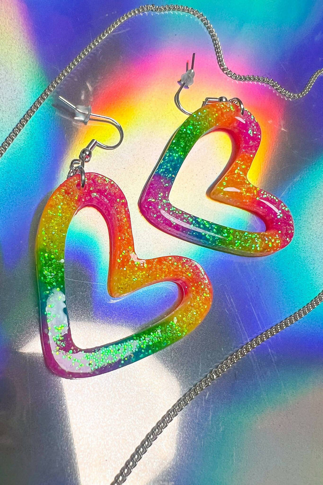 Close-up of rainbow heart earrings with glitter on holographic background