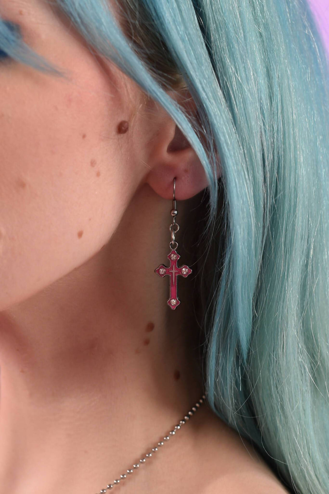 Close-up of pink crystal crucifix earring on ear