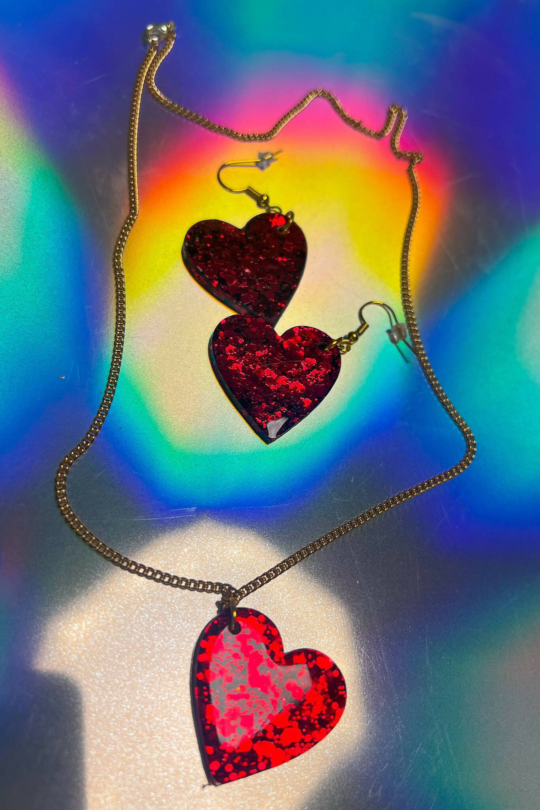 Red glitter heart necklace and earrings with rainbow reflection.