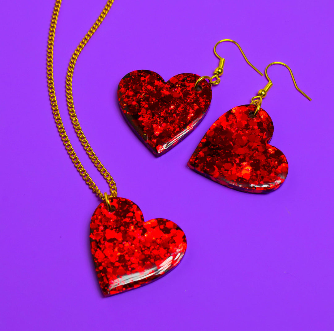 Red glitter heart resin earrings and necklace on purple background.