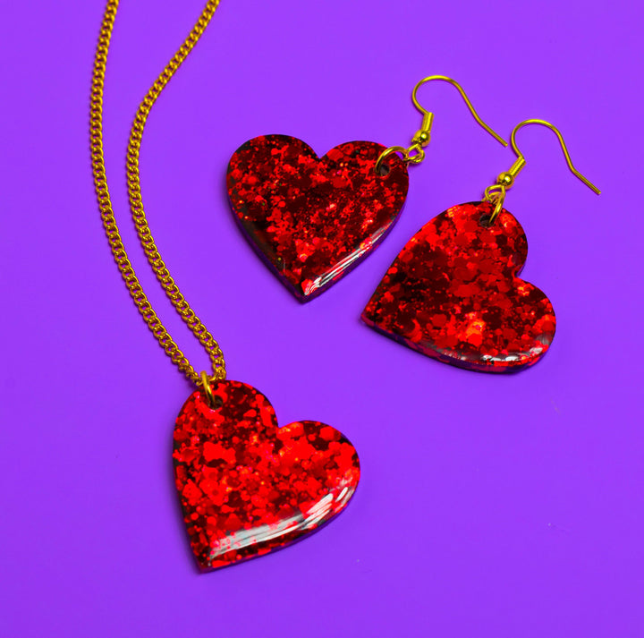 Red glitter heart resin earrings and necklace on purple background.