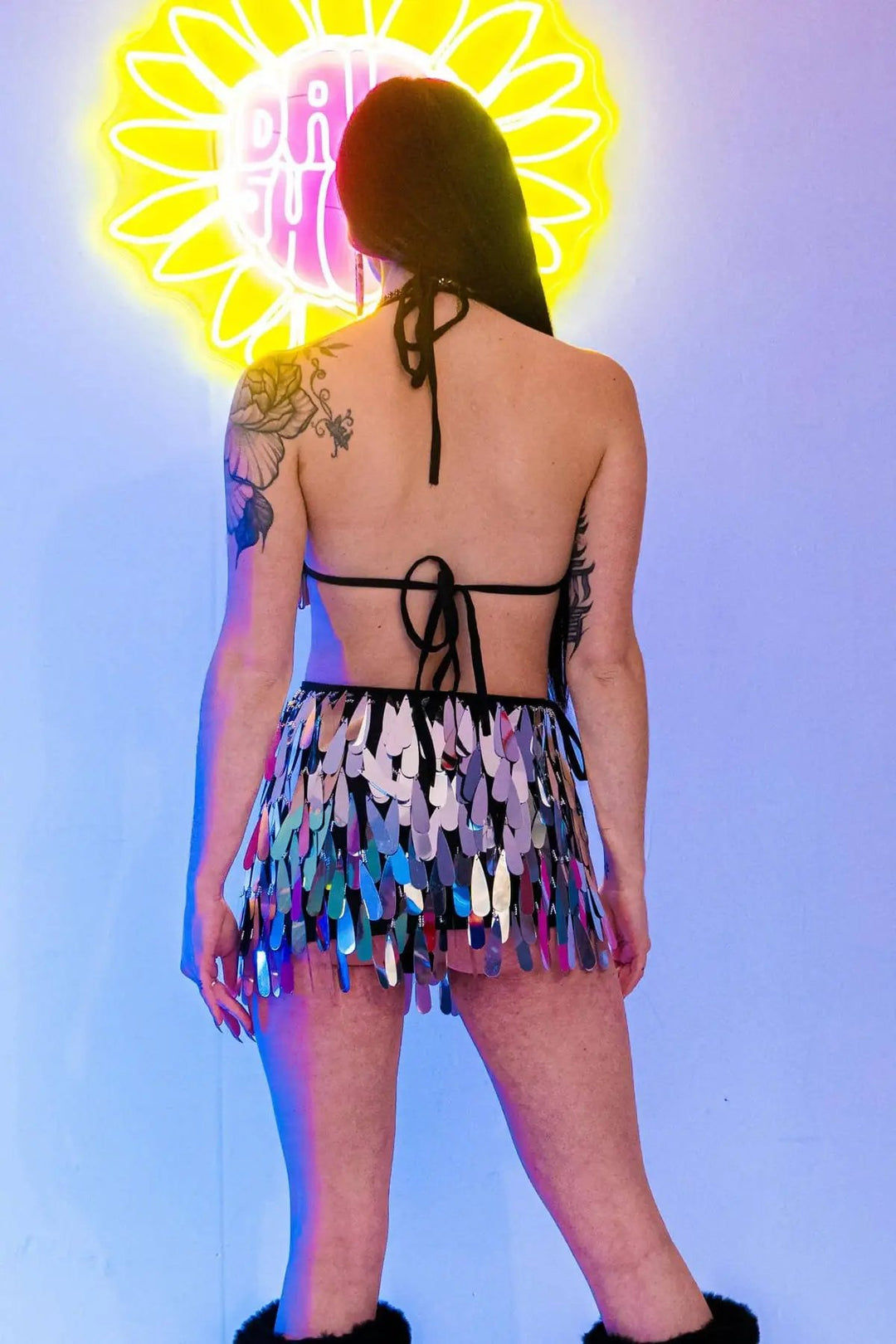 Back view of silver sequin skirt, neon daisy sign.