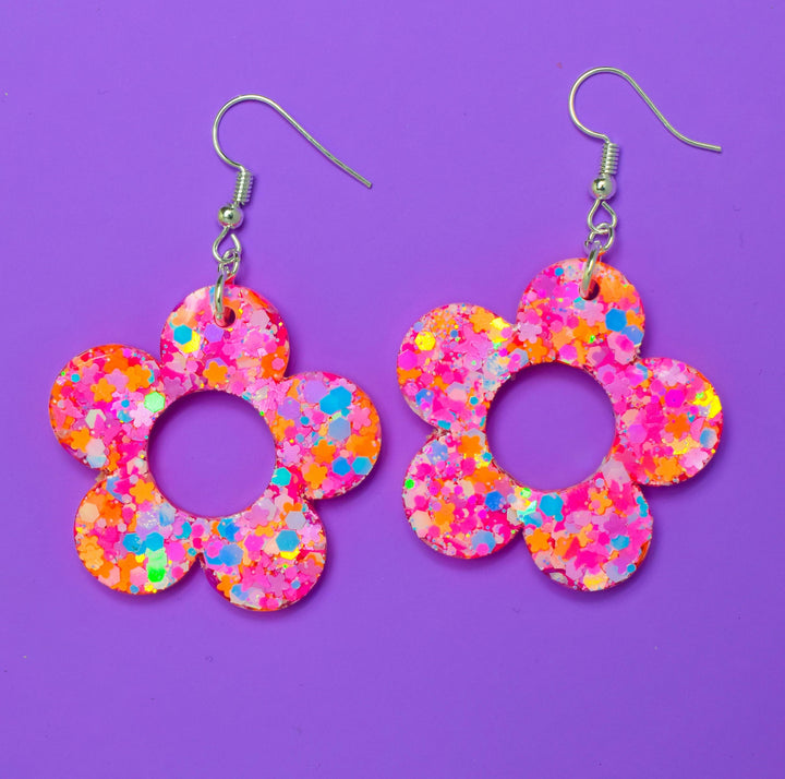 Glittery resin flower earrings on purple background