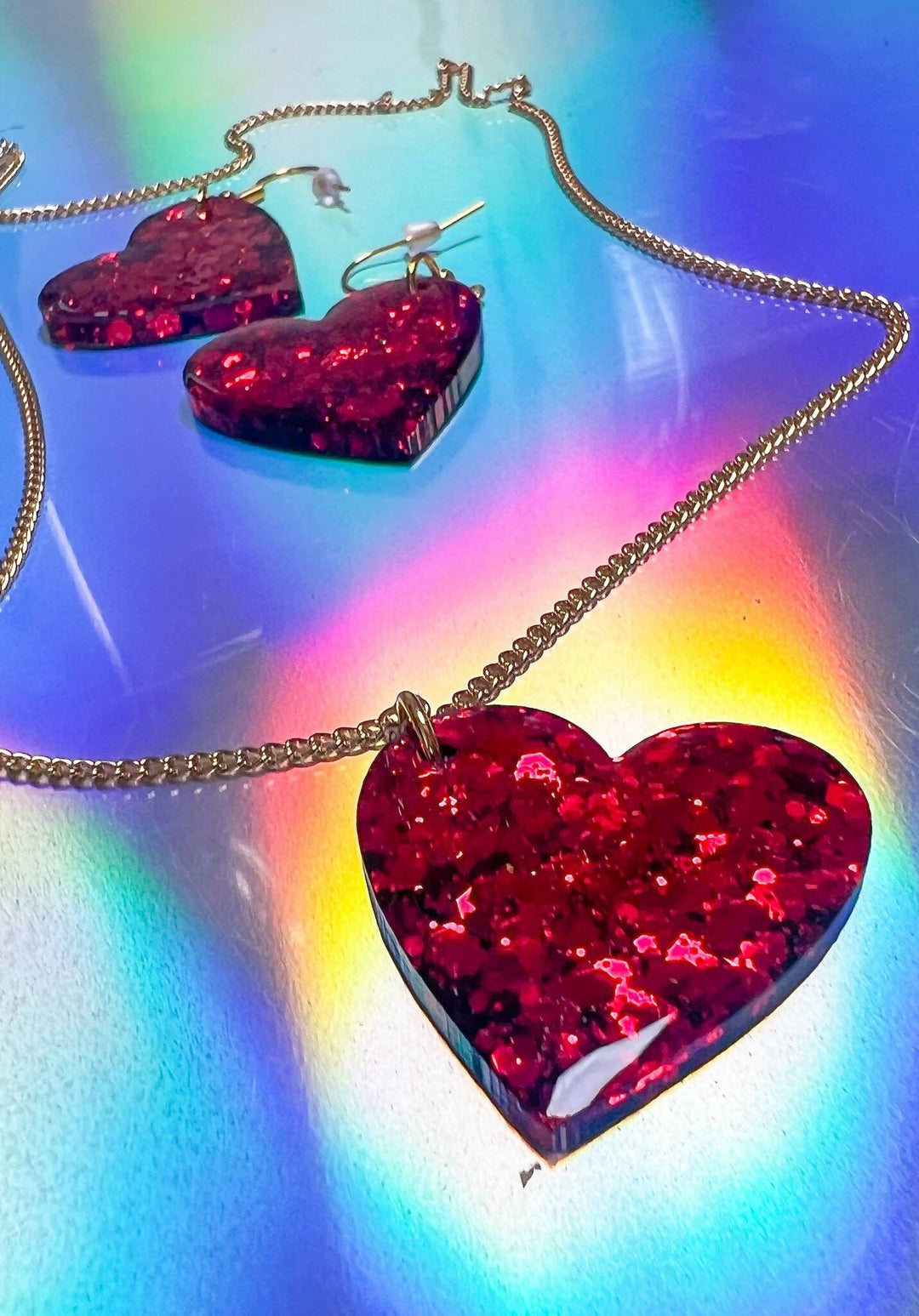 Red glitter heart necklace and earrings on rainbow background.