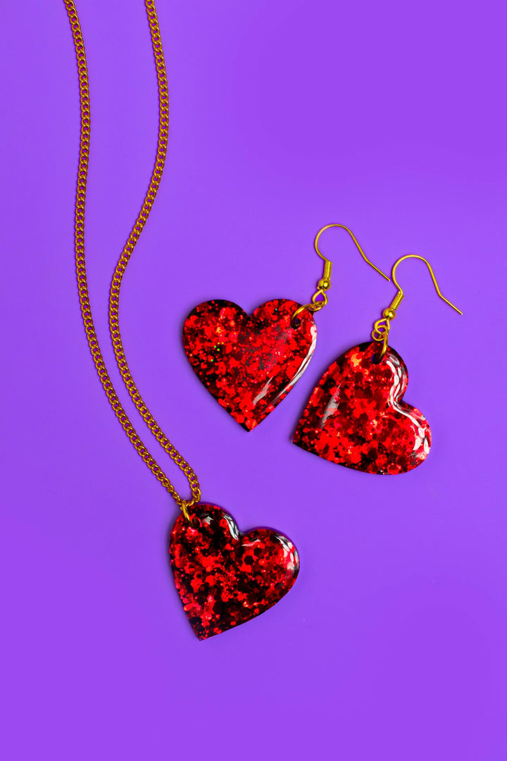 Heart-shaped red glitter resin jewelry set on purple surface.