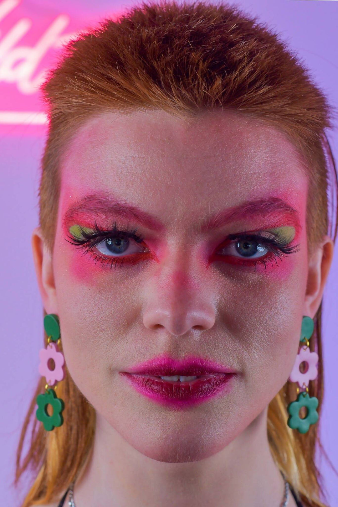 Model wearing pink and green daisy earrings, bold makeup