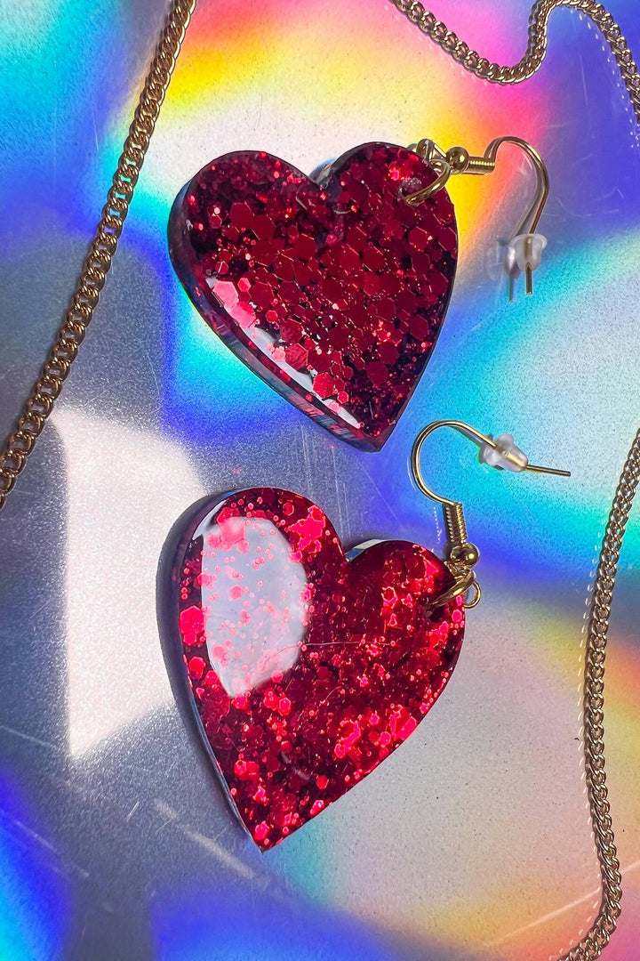 Close-up of red glitter heart earrings on rainbow surface.